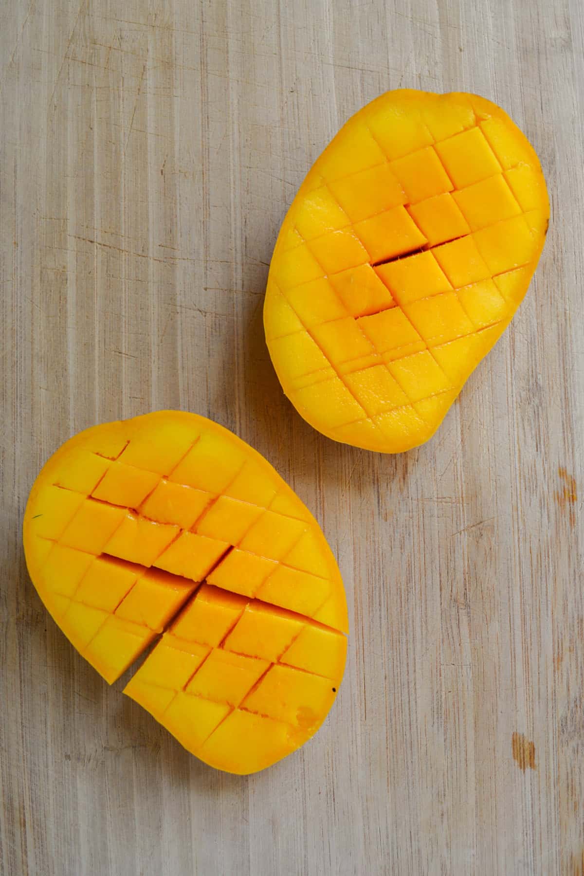 Mango cheeks that have been scored on a cutting board.