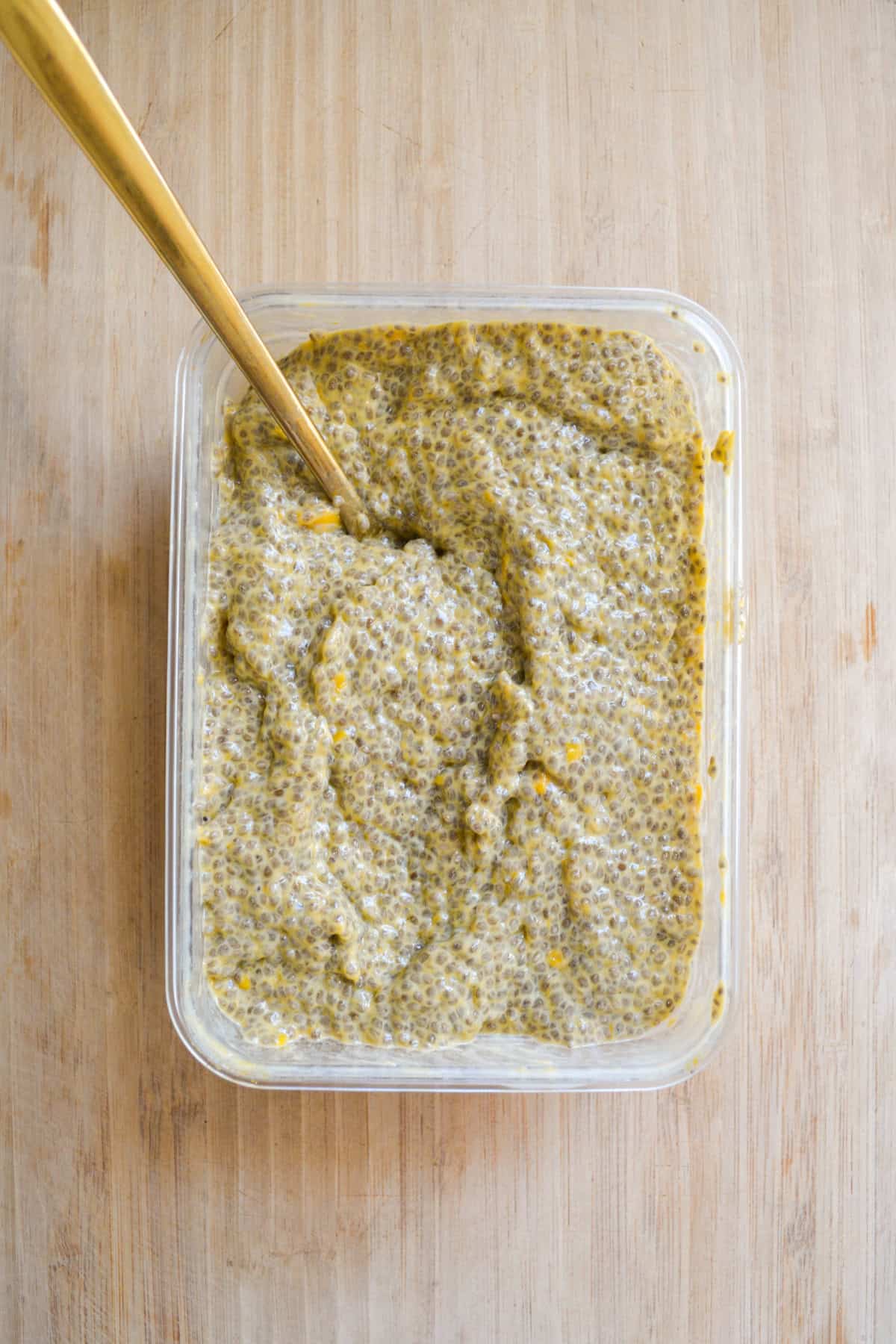 Mango Chia Seed Pudding that has been soaked overnight in a container with a spoon.