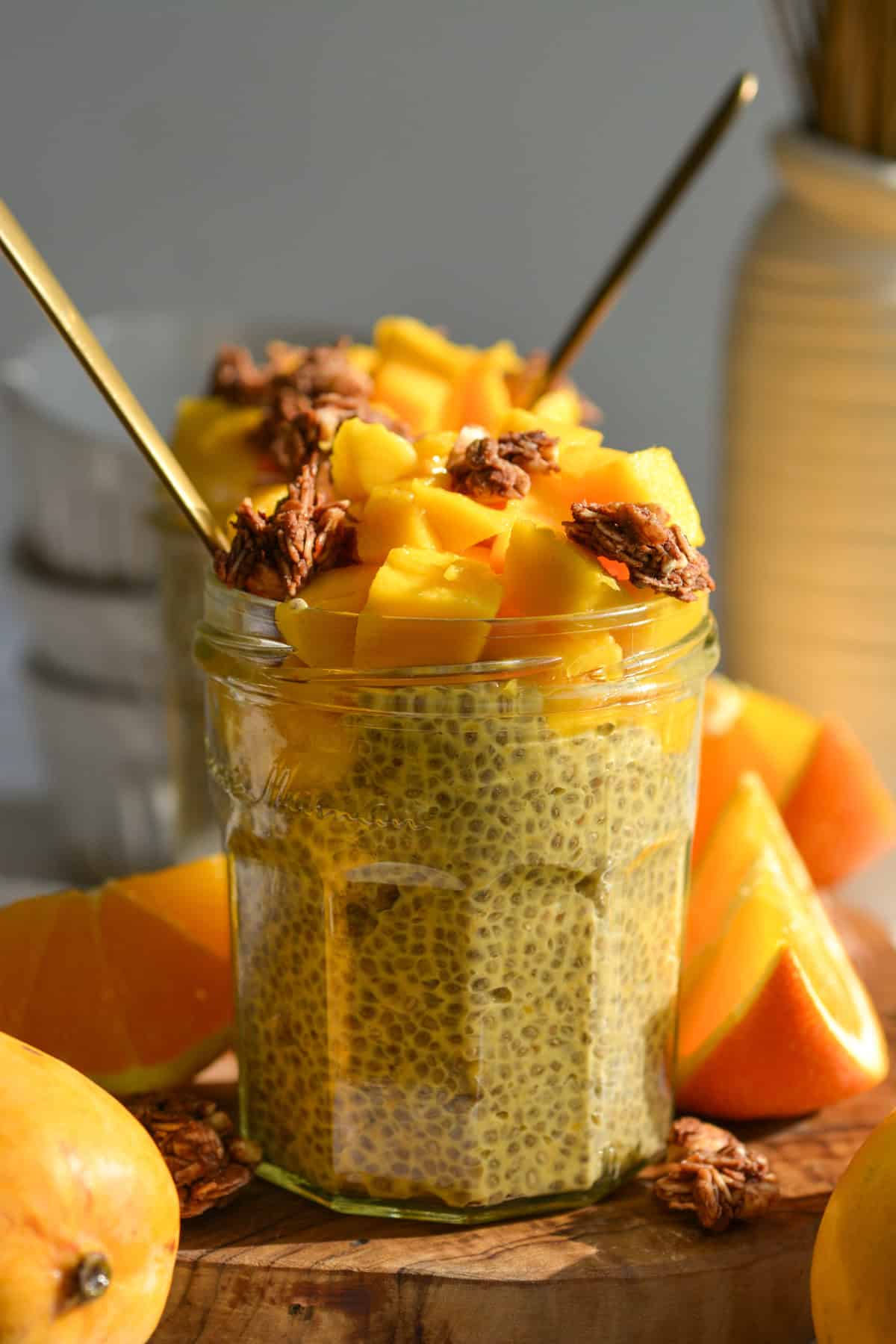 Two jars of mango chia seed pudding topped with mango chunks and granola on a wooden board.