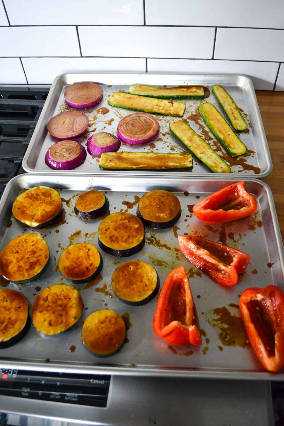Vegetables that have been brushed in balsamic and olive oil on sheet trays.