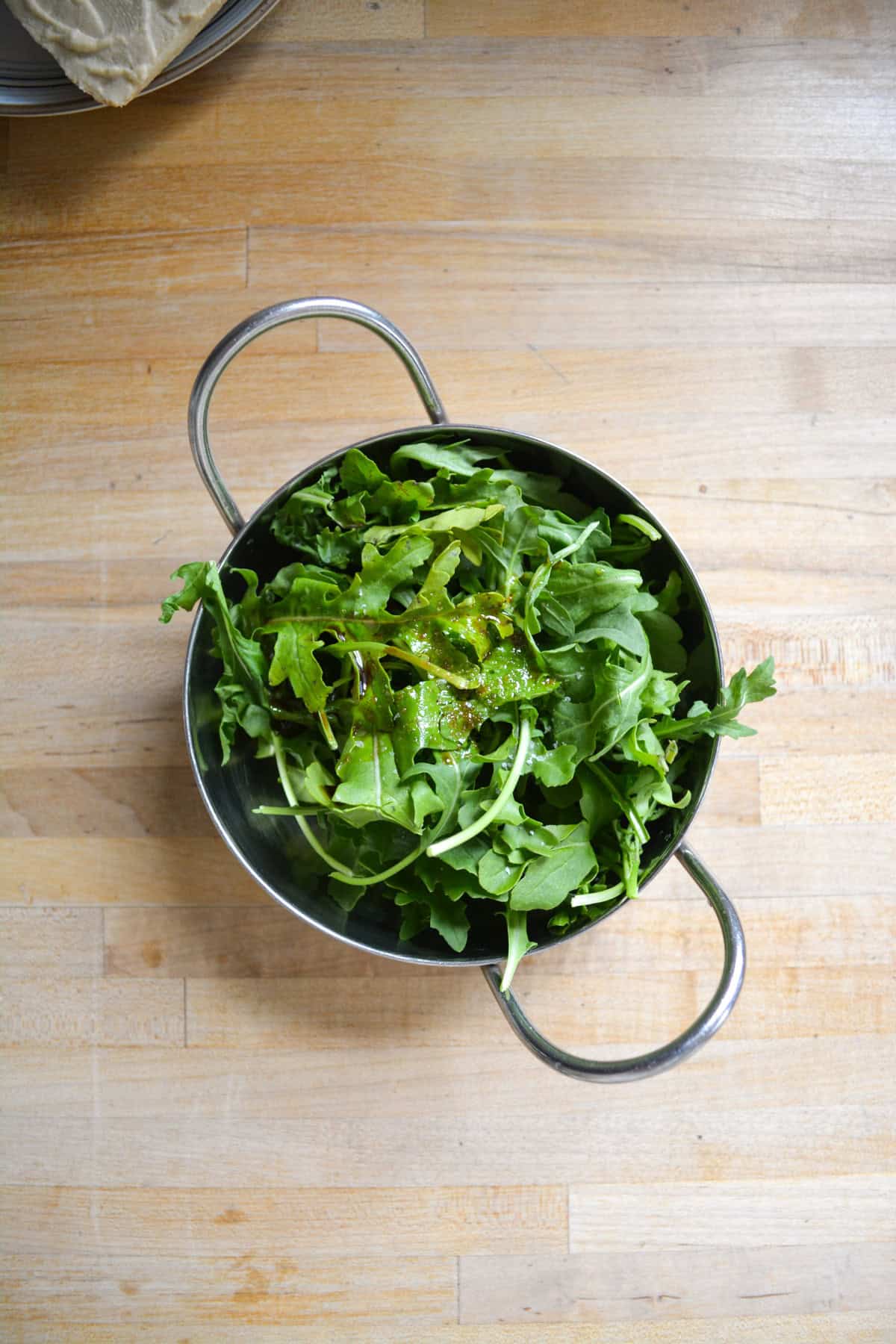 Arugula with oil and vinegar on it. in a small metal bowl.