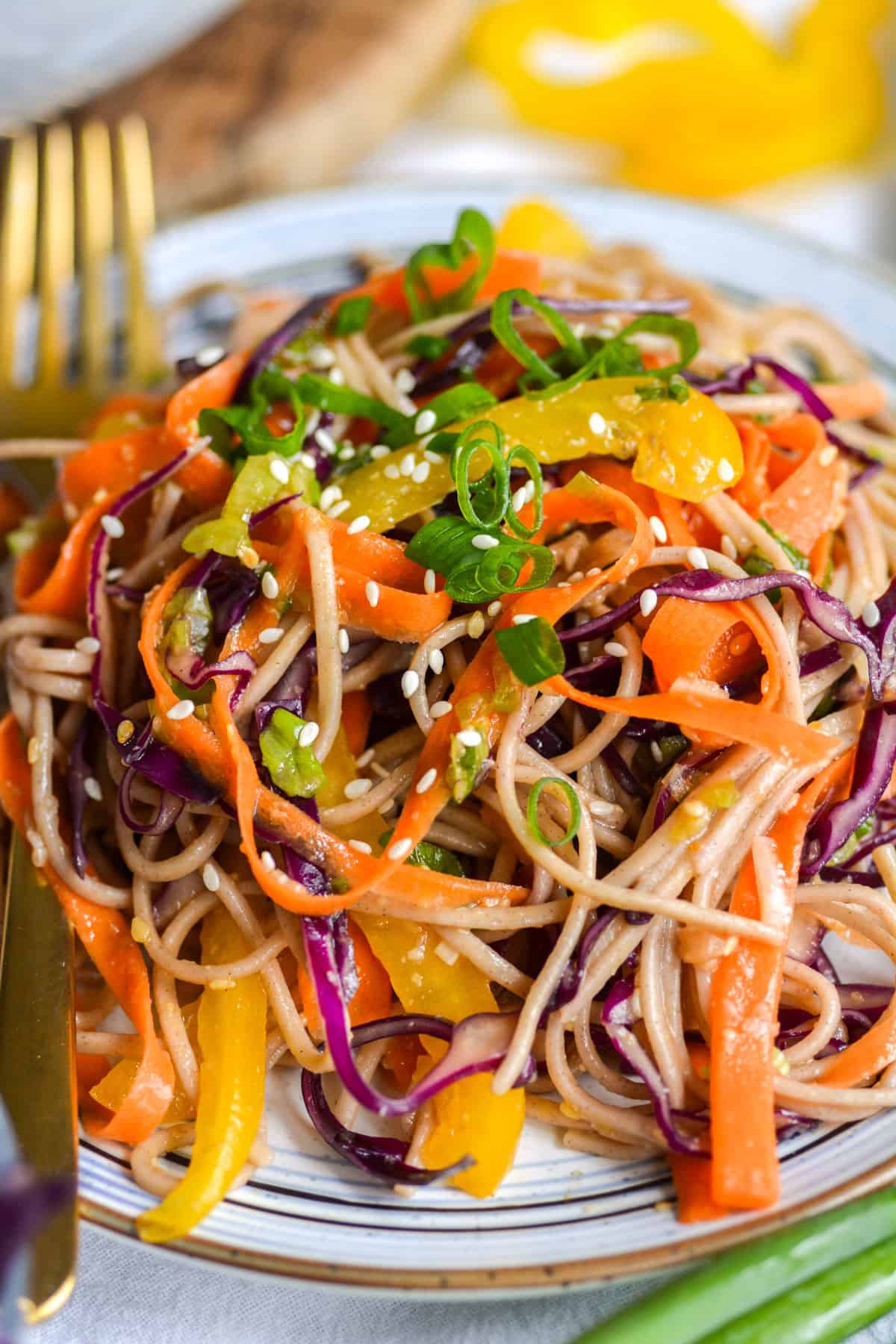Soba noodle salad on a plate topped with scallions and sesame seeds.