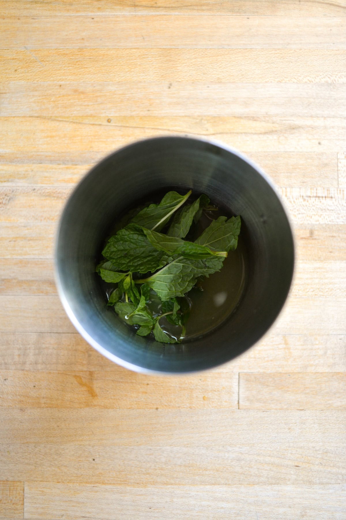 Mint leaves and juice in a metal cocktail shaker.