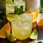 A glass filled with Tequila Smash cocktail and ice sitting on a small wooden board.