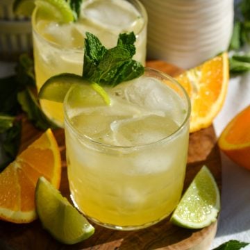 A glass filled with Tequila Smash cocktail and ice sitting on a small wooden board.