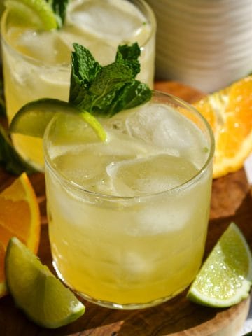 A glass filled with Tequila Smash cocktail and ice sitting on a small wooden board.