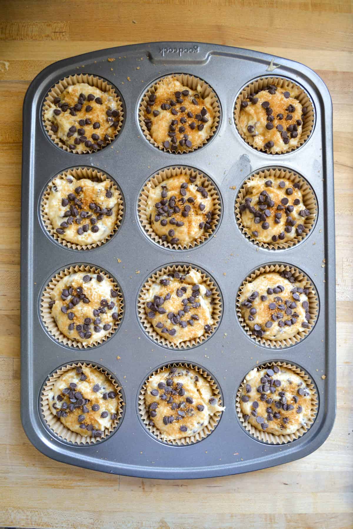 Muffin batter scooped into a lined muffin tin topped with sugar and extra chocolate chips.