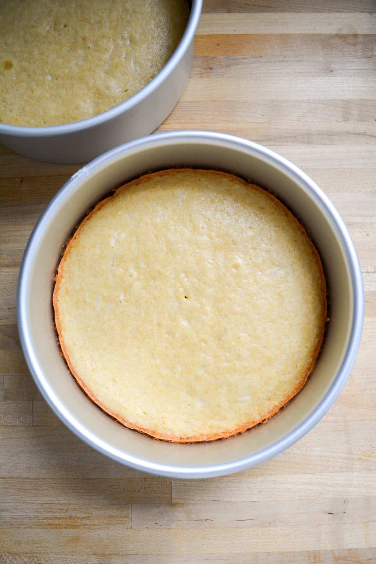 Two baked cakes in round pans on a wooden surface.