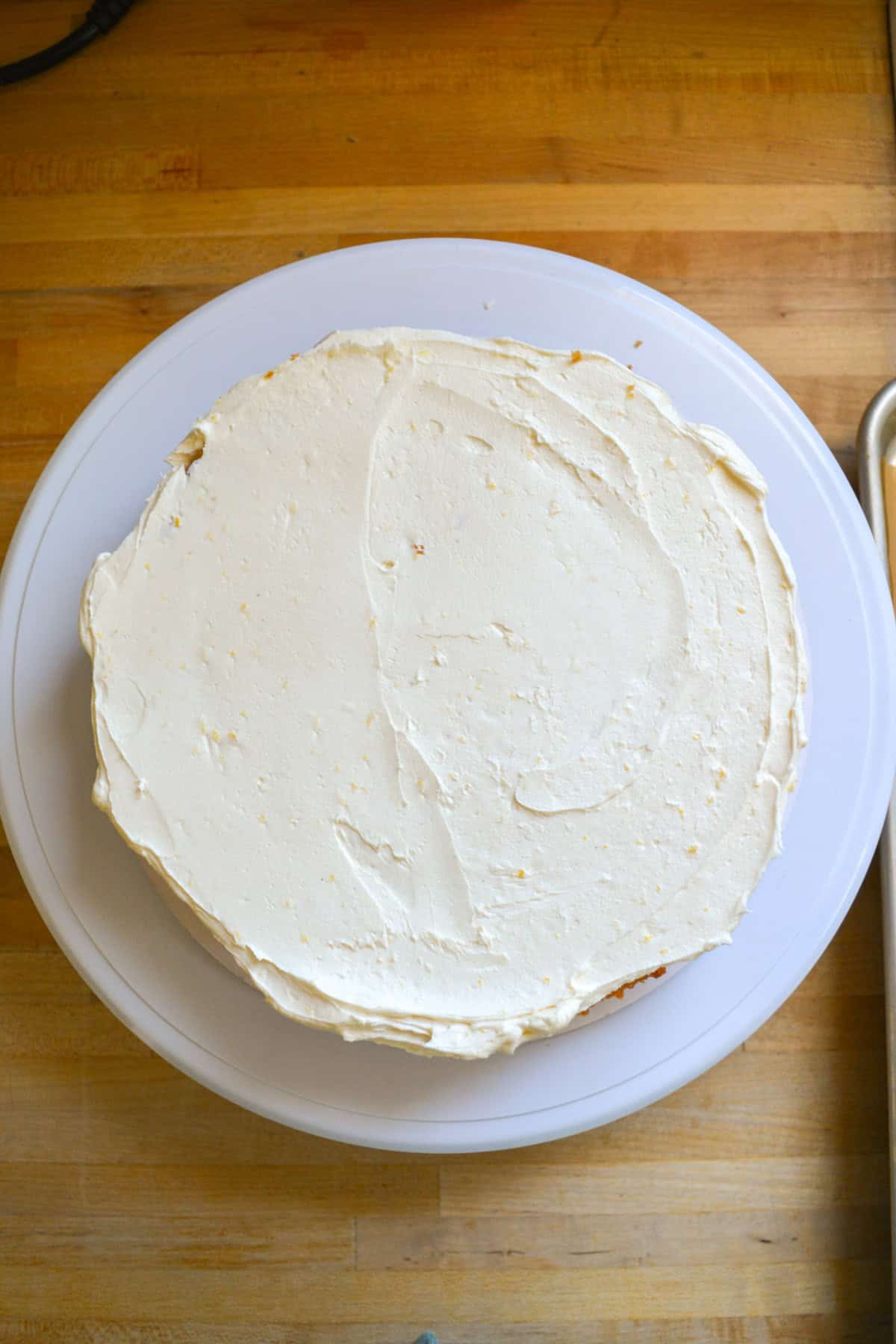 A cake layer on a cake board with lemon frosting spread on top.