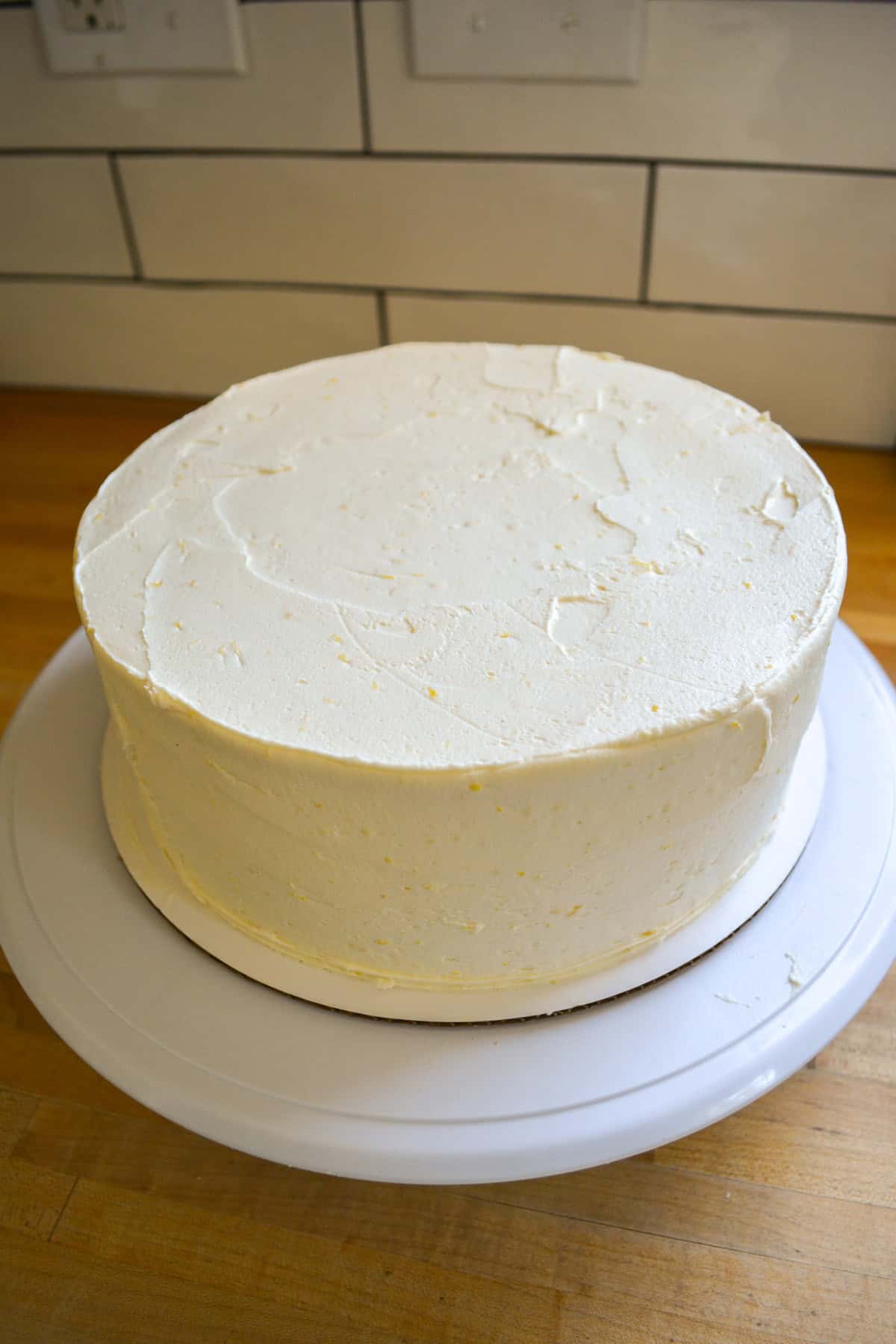 Frosted vegan lemon cake on a turn table.