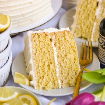 A slice of Vegan Lemon Cake on a plate next to a bowl of sliced lemons.