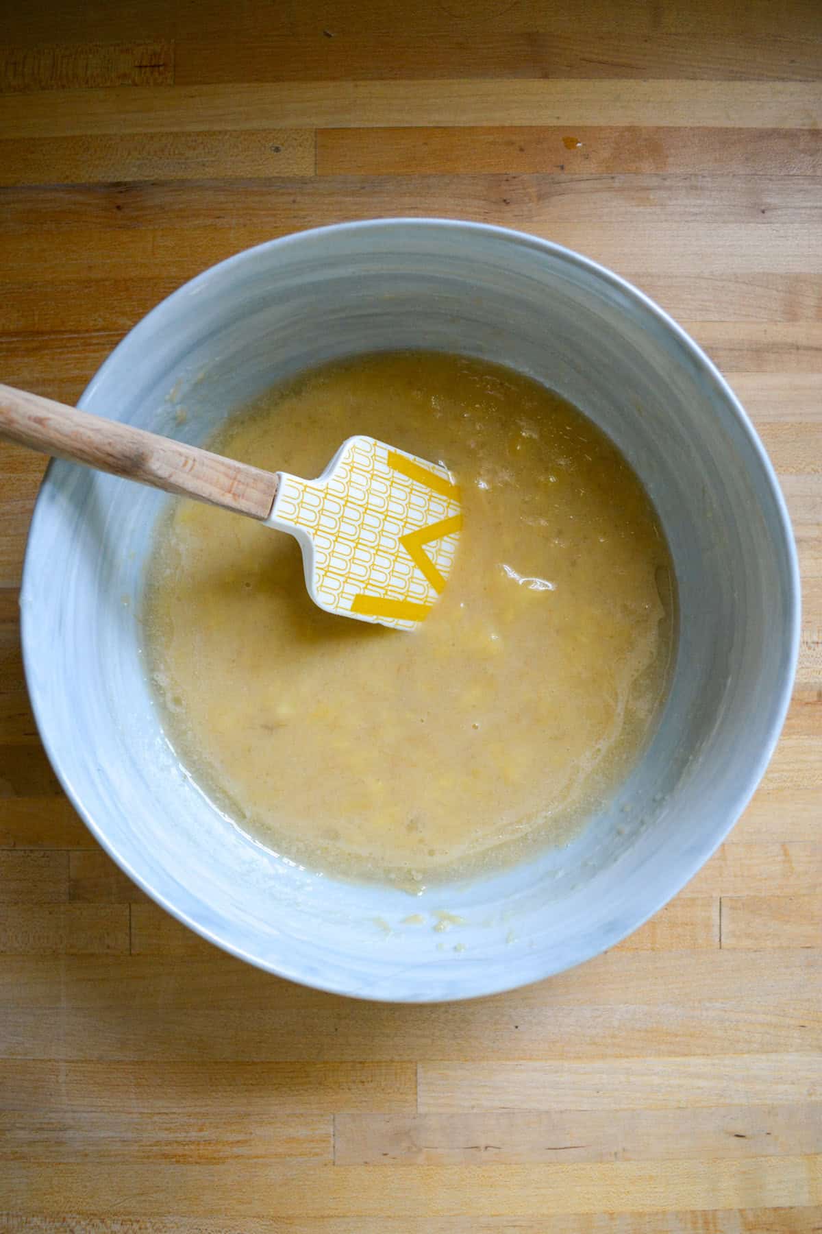 Mashed banana in a mixing bowl with a rubber spatula.
