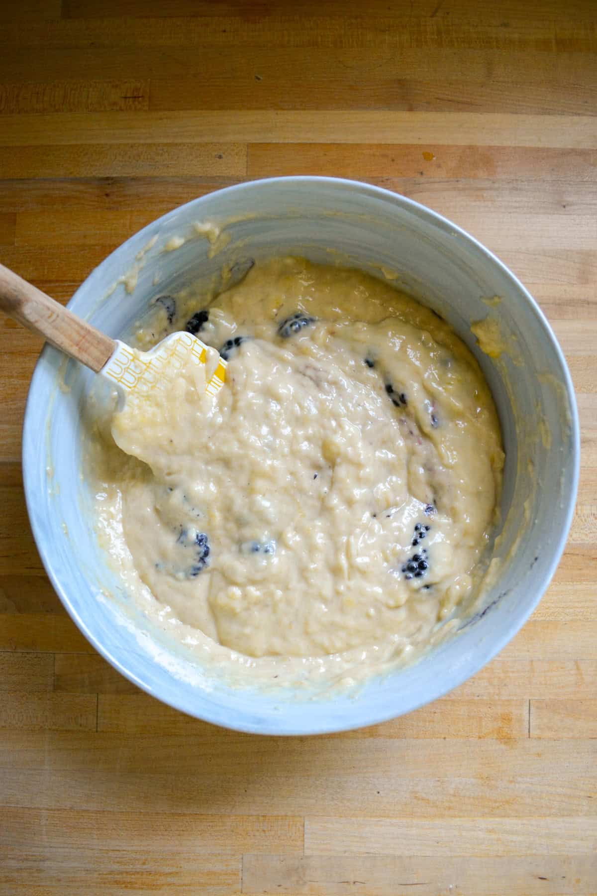 Blackberries mixed into banana bread batter in a large mixing bowl.
