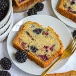 A slice of Blackberry Banana Bread on a small plate next to a gold fork.