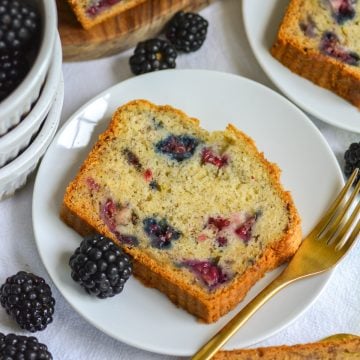 A slice of Blackberry Banana Bread on a small plate next to a gold fork.
