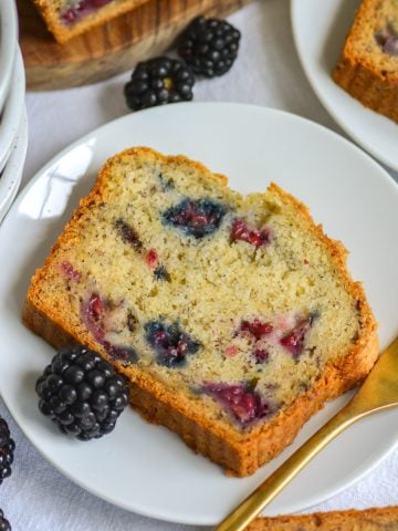A slice of Blackberry Banana Bread on a small plate next to a gold fork.