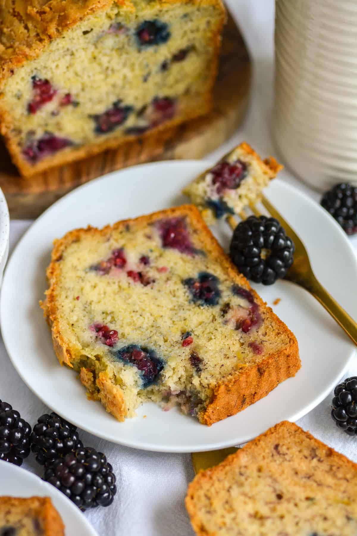 A slice of Blackberry Banana Bread on a small plate with fresh blackberries in the scene.