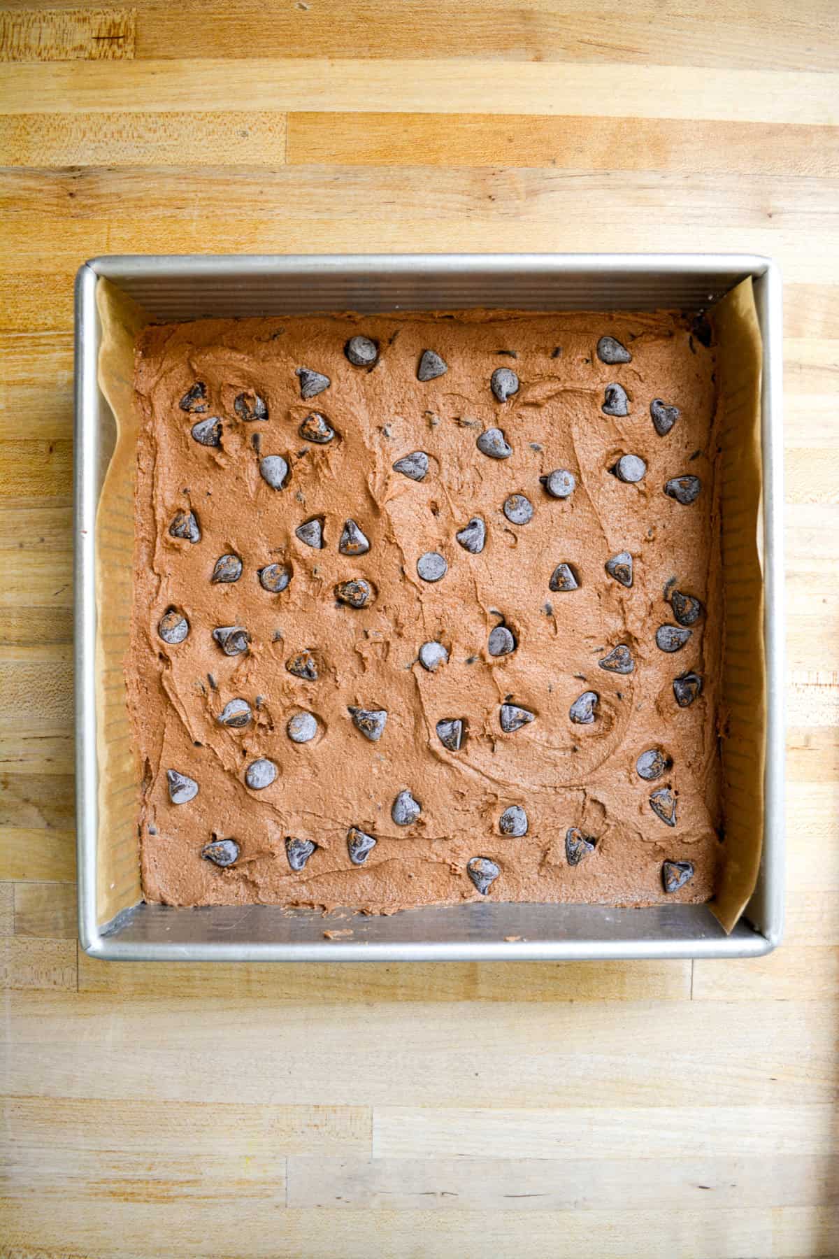 Cookie dough in a square pan topped with chocolate chips.