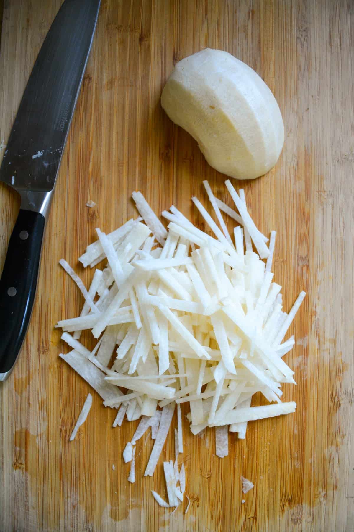 A jicama sliced into match sticks on a wooden cutting board.