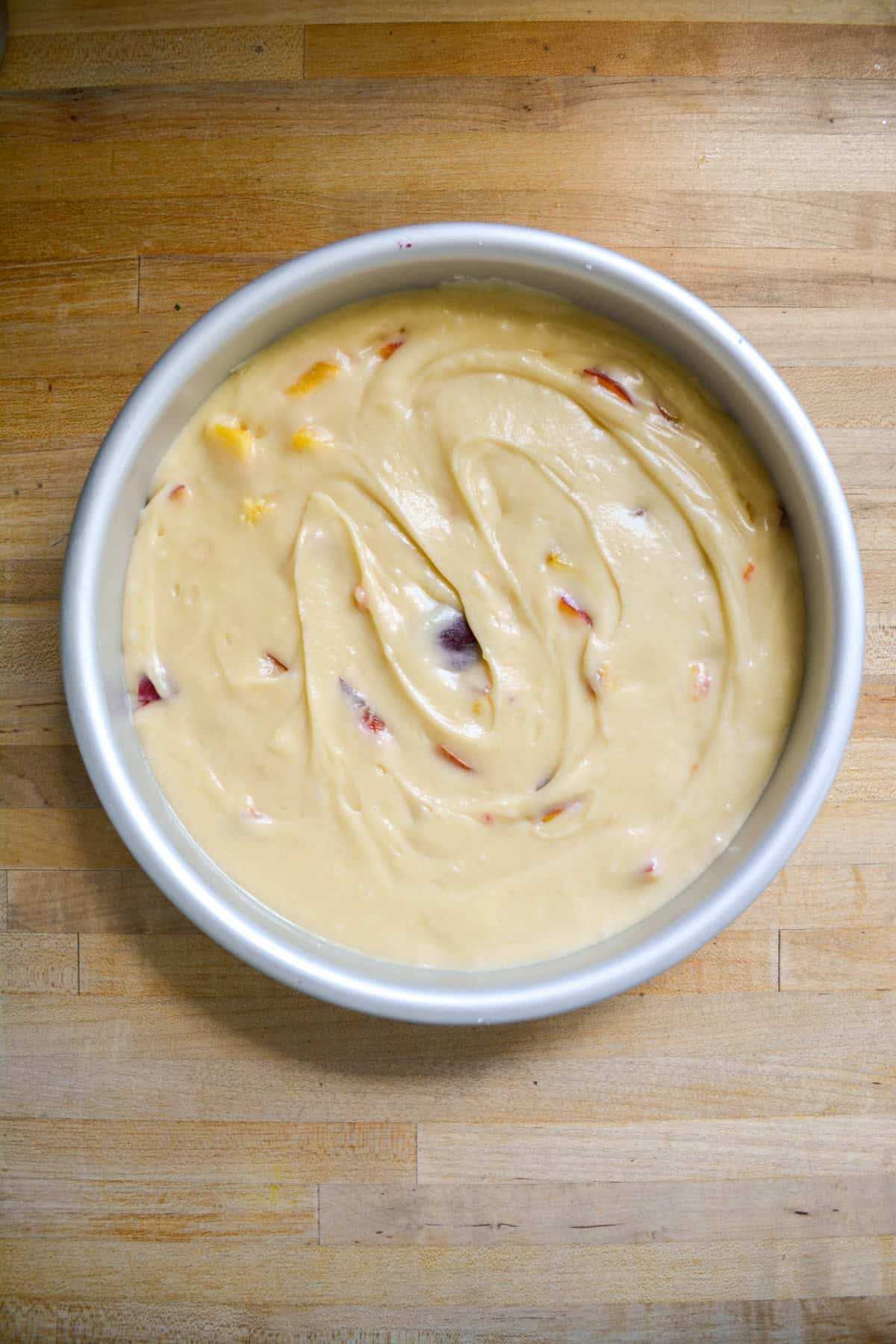 Cake batter with peaches in it in a round cake pan.