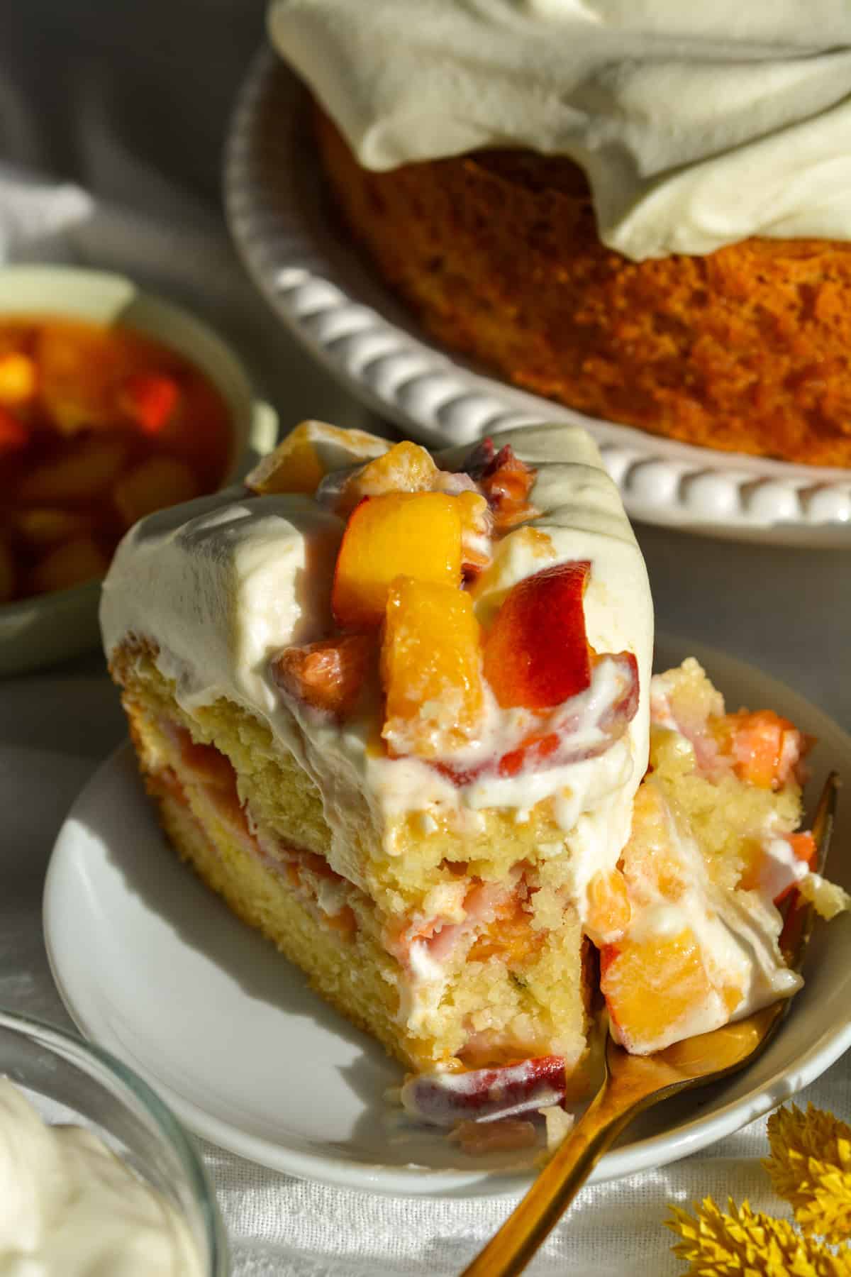 A slice of Vegan Peaches and Cream Cake on a small plate with a bite taken out of it.