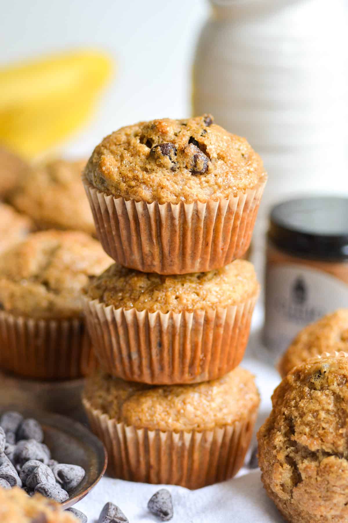 Three Vegan Banana Muffins stacked on top of each other with chocolate chips in the foreground.