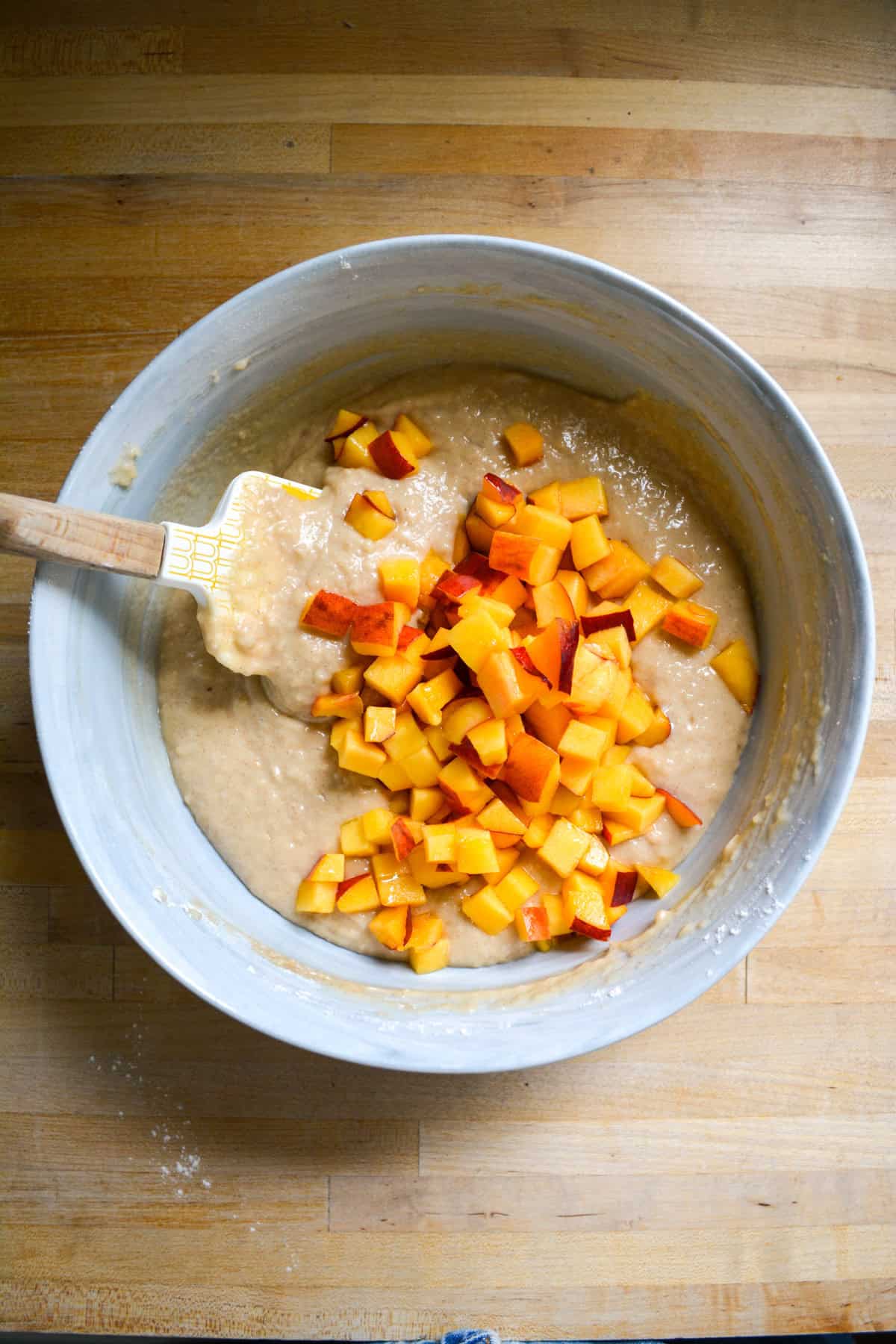 Chopped peaches added to vegan muffin batter in a large bowl.