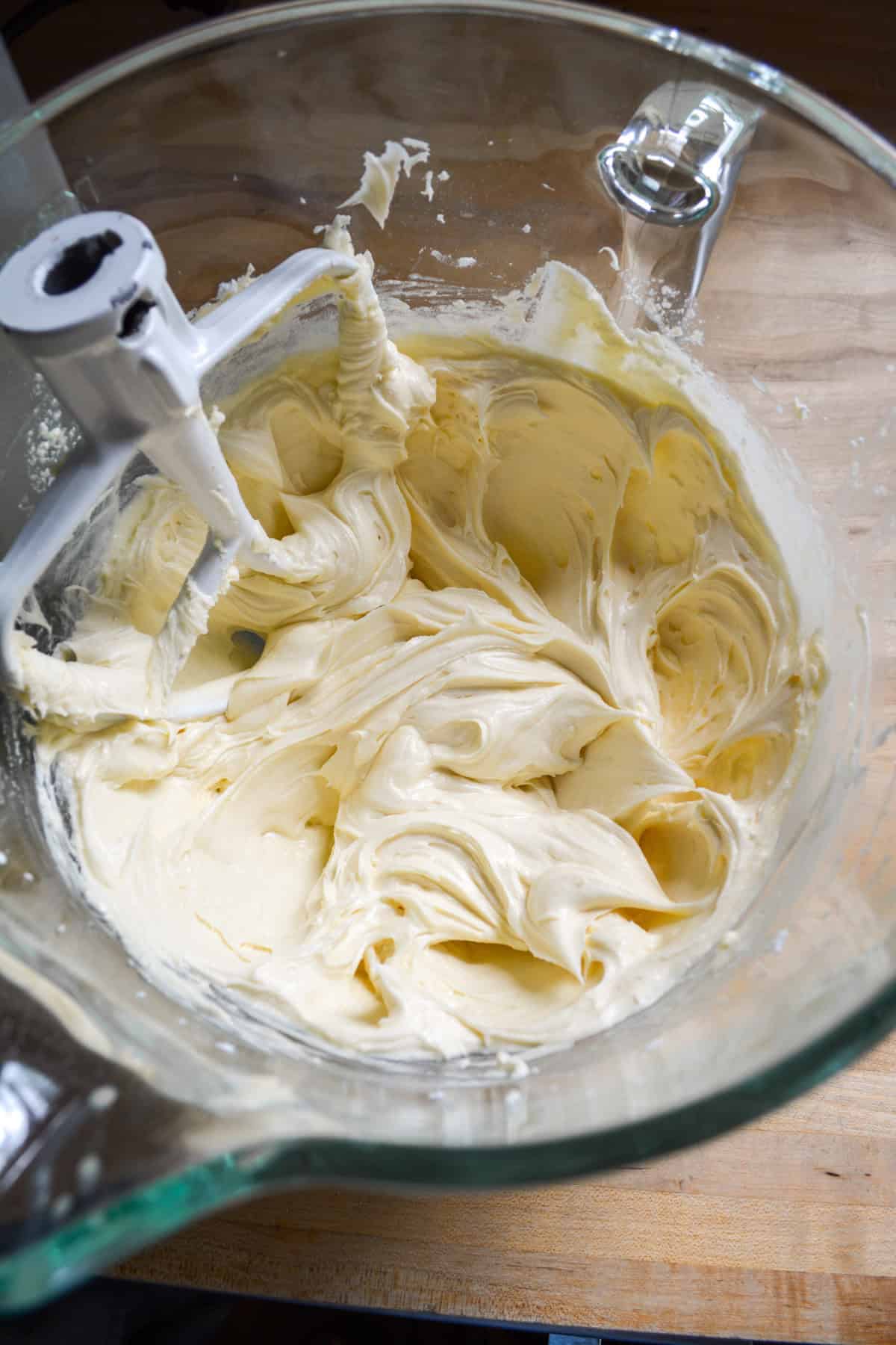 Non-dairy milk and vanilla added into the frosting in a glass bowl.