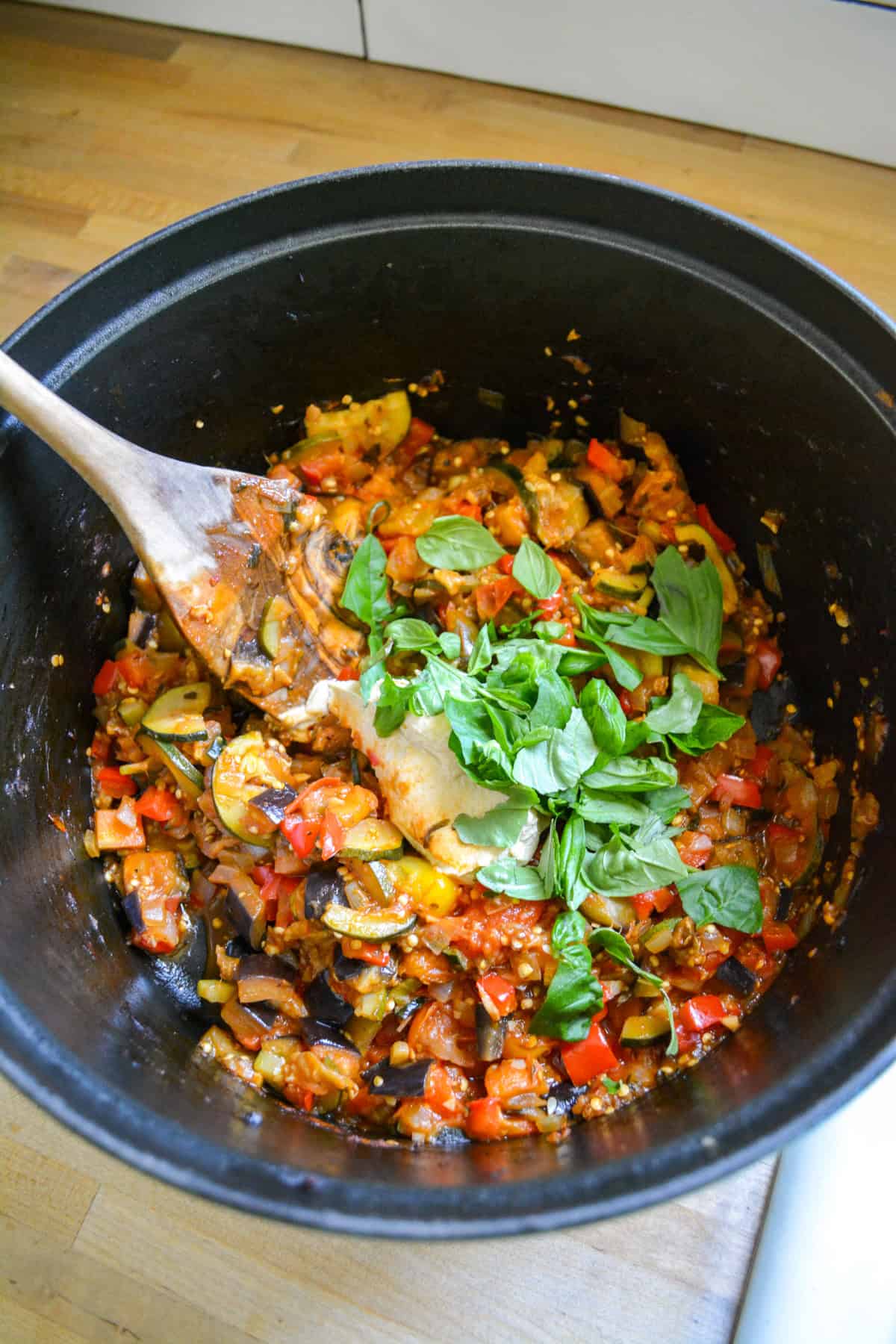 Roasted vegetables in a Dutch oven with hummus and basil.