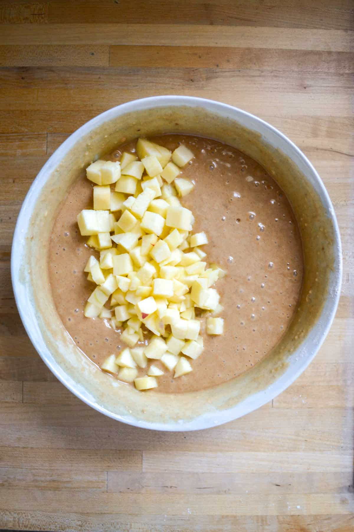 Vegan cake batter with chopped apples added in a large bowl.