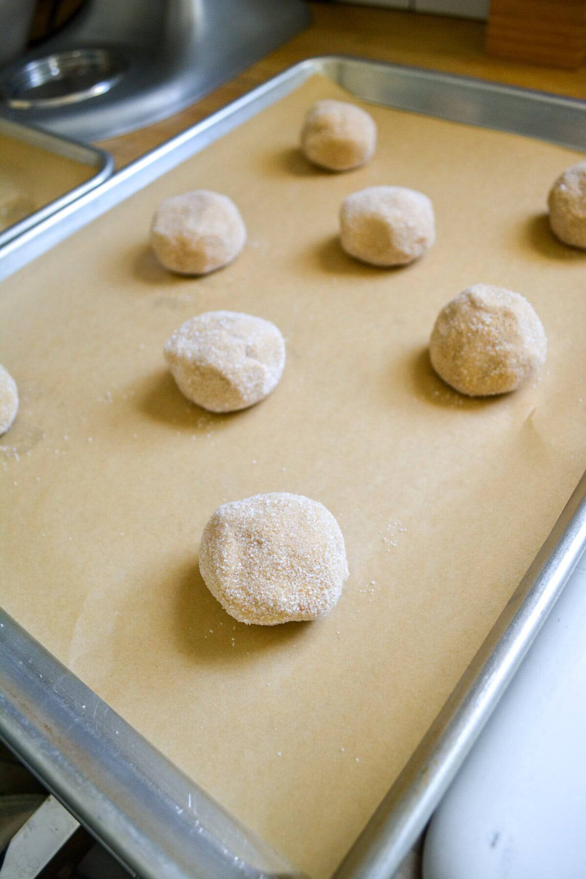 Cookie dough balls rolled in granulated sugar on a baking sheet.