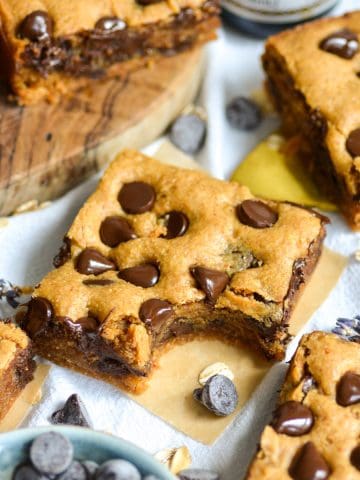 A Gluten-Free Peanut Butter Blondie with a bite taken out of it on a square of parchment.