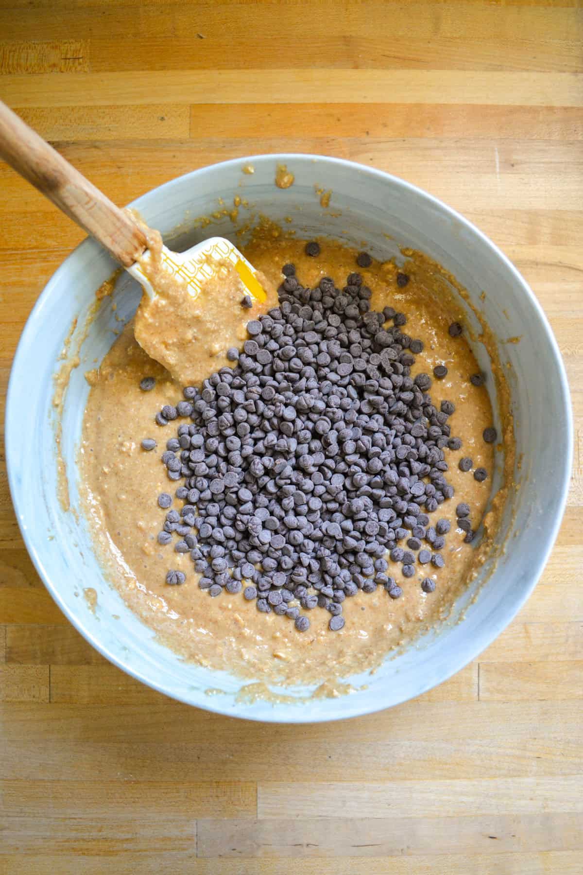 Mini chocolate chips in oat flour muffin batter in a large mixing bowl.