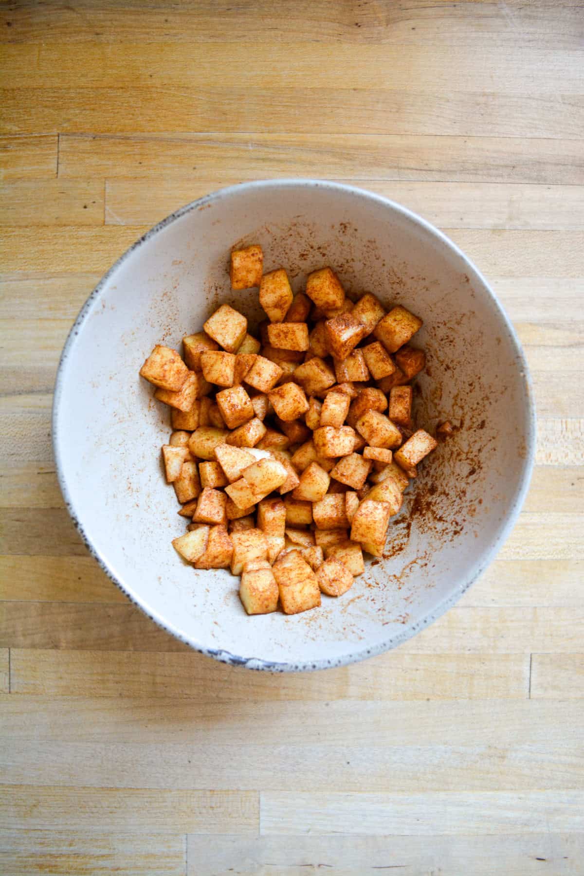 Chopped apples tossed with cinnamon in a bowl on a wooden surface.