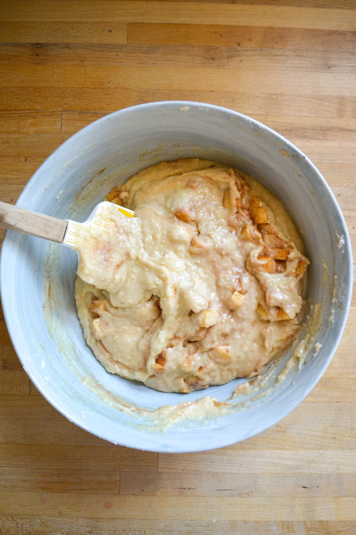 Cinnamon apples folded into crumb cake batter in a large bowl.