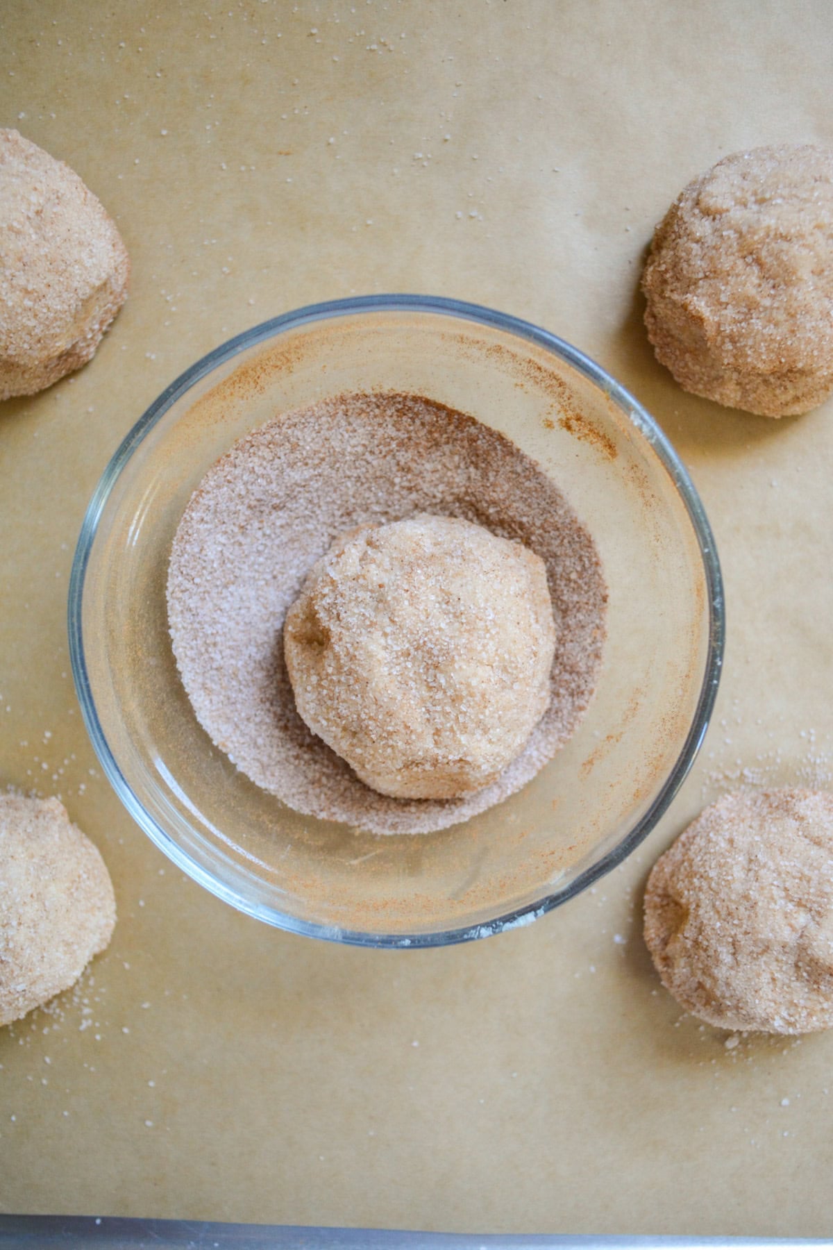 A cookie dough ball in a small bowl of cinnamon sugar.